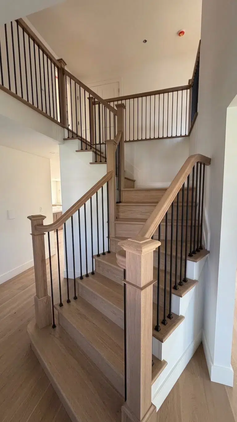 Staircase with light oak treads and risers, a white open stringer, oak handrails and newels, and black metal balusters in a Bay Shore, NY home