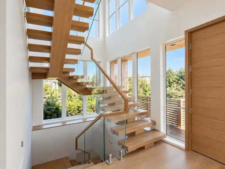 Open riser staircase with a light wood center stringer, glass railing and wood handrail in a Westhampton Beach, NY home